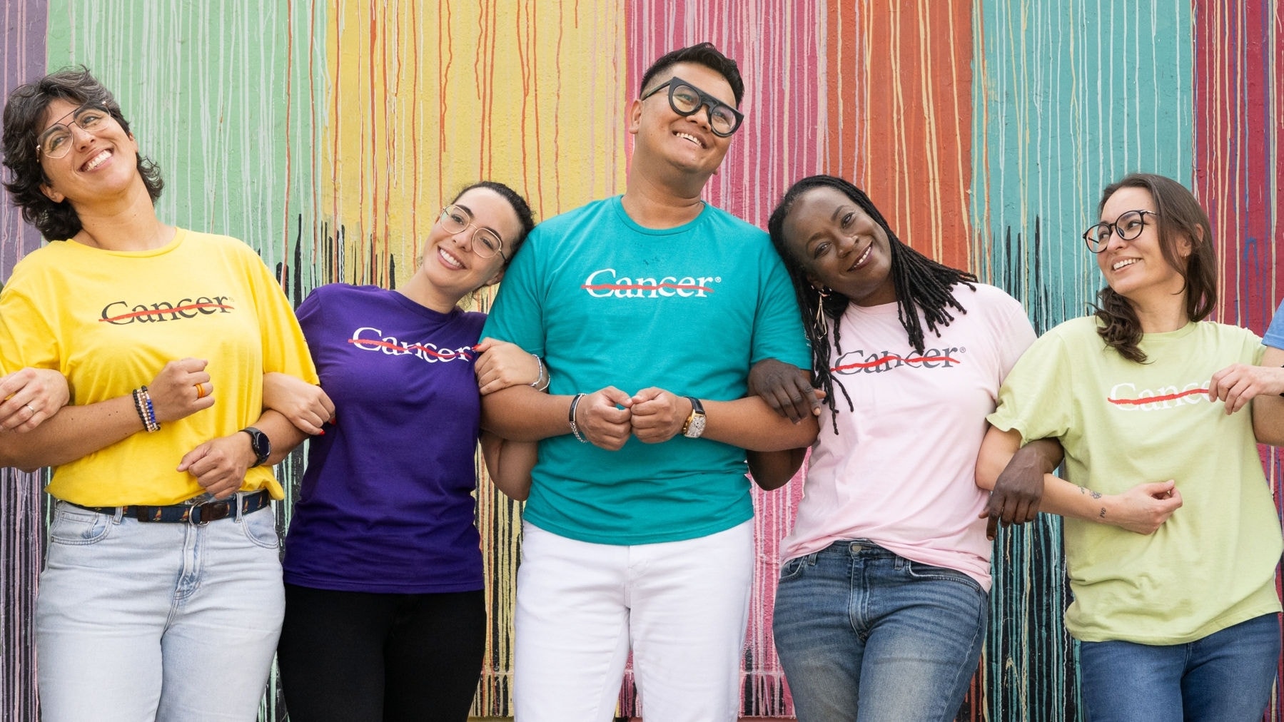 A group of five smiling people in multi-colored strikethrough t-shirts